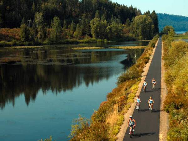 Bicyclists on a long narrow bike trail riding next to a beautiful river