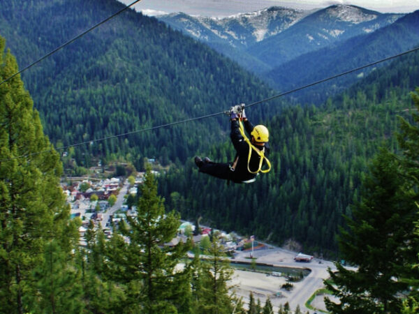 Man zip lining in Wallace, Idaho. Green trees and mountains in the distance.