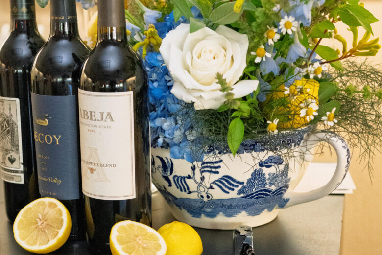 Three wine bottles, flowers and lemons sitting on a table